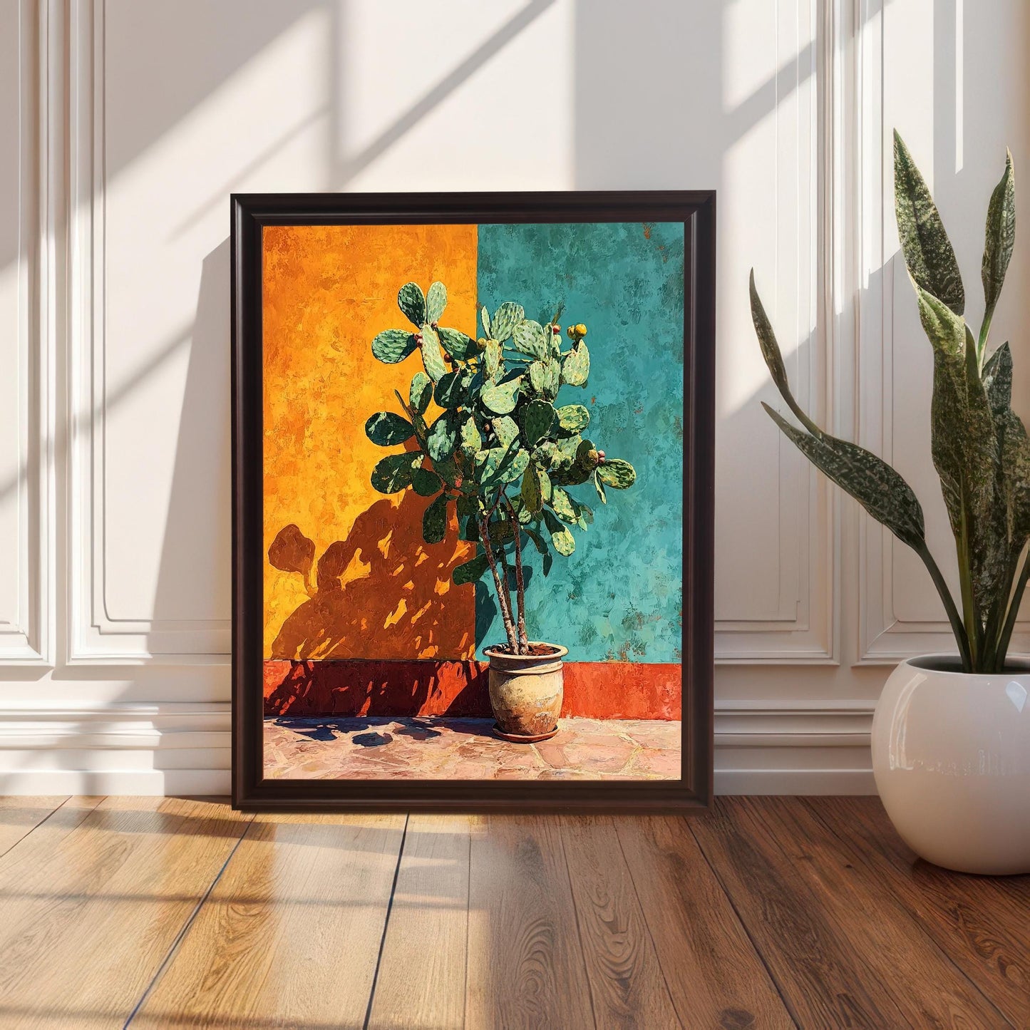 The vibrant cactus art print in a Black Wood Frame with no mat, leaning on a glossy wood floor against a white wainscoted wall. Sunlight streams across the floor, highlighting a potted snake plant on the right.