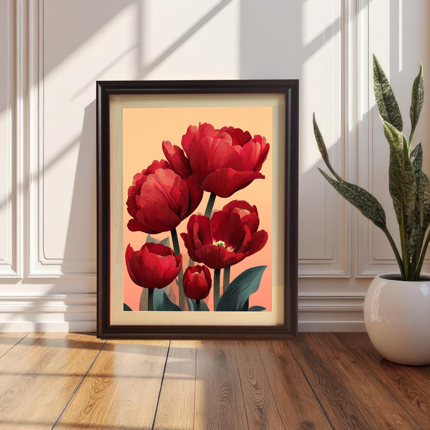 A framed print of the red tulip art in a Coffee/Dark Brown Frame with a Mount (matting). The frame is leaning against a white wainscoting wall on a wood floor, next to a potted snake plant.