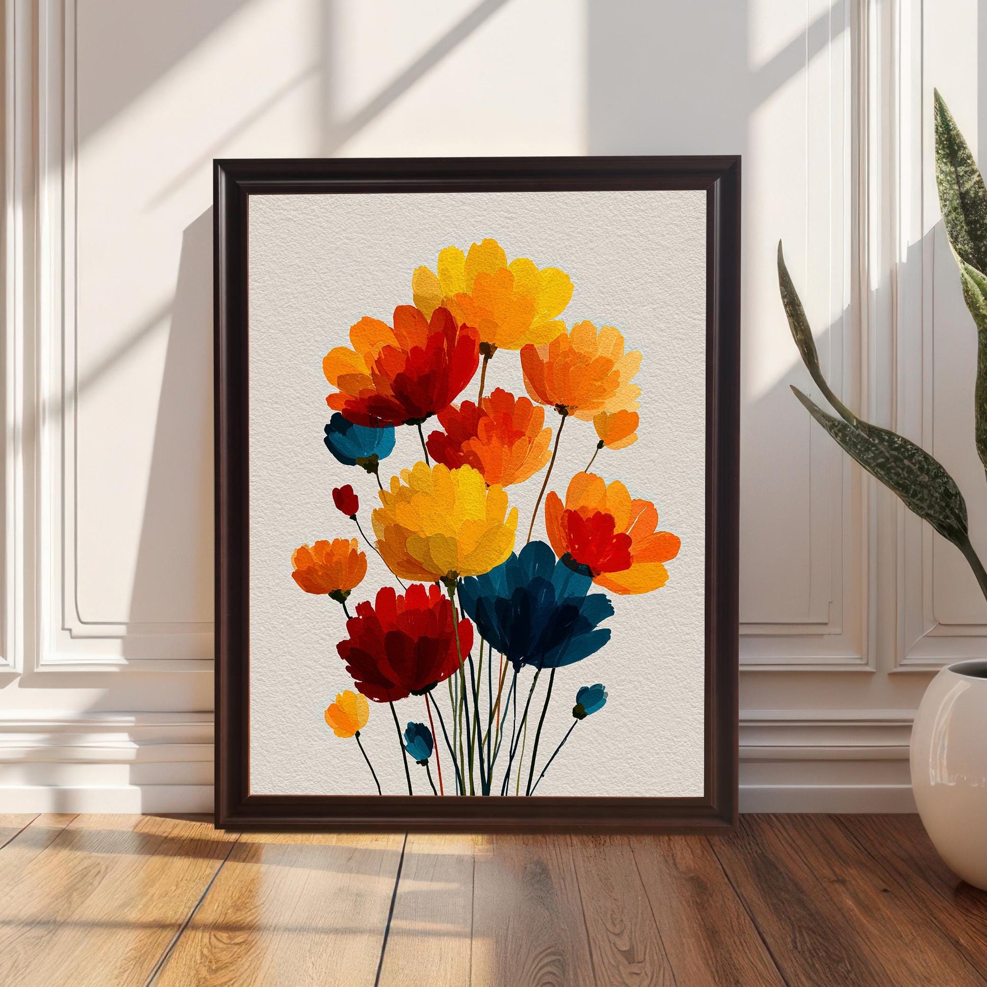 The abstract floral art print with red, orange, yellow, and blue flowers, displayed in a Coffee-colored wood frame, resting on a wooden floor against a white paneled wall next to a potted snake plant.