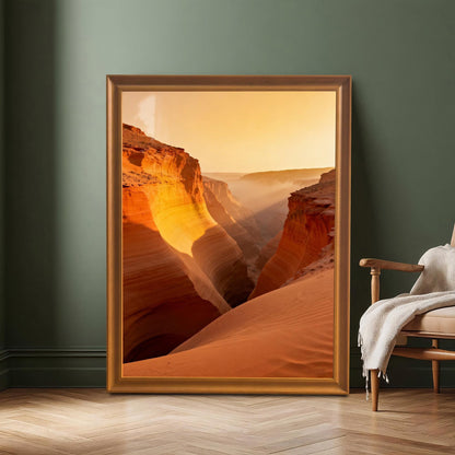Large framed print of the orange and red canyon landscape resting on a wood floor against a dark green wall, next to a wooden armchair. The frame is Orange-colored wood.