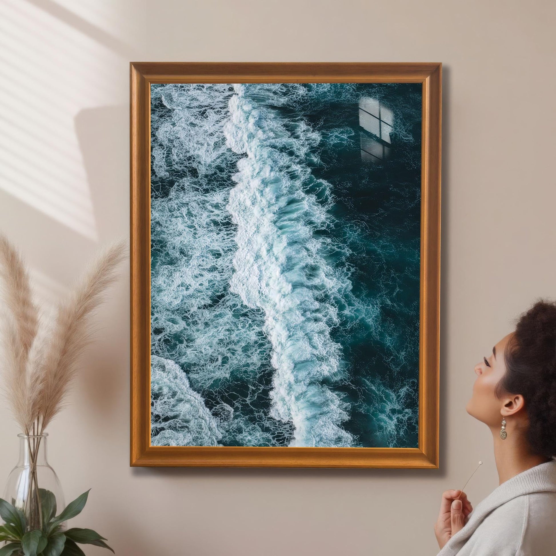 Large, portrait-oriented framed print of an ocean wave with an Orange/Gold frame, hanging on a beige wall in a home setting with a person looking up at it.