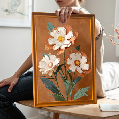 Lifestyle photo where a person is holding the framed print, showing the Orange wood frame. The artwork is a vibrant, textured illustration of three flowers on a terracotta background.