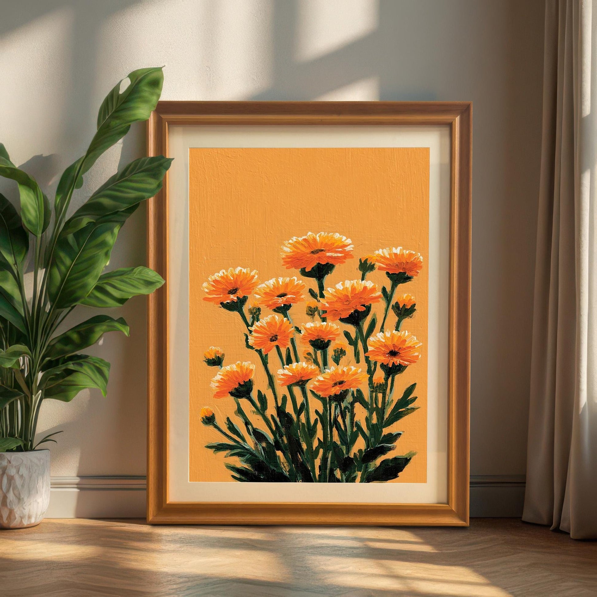 A portrait-oriented orange floral art print in an Orange wood frame leaning on the floor against a white wall next to a potted green plant and curtain.