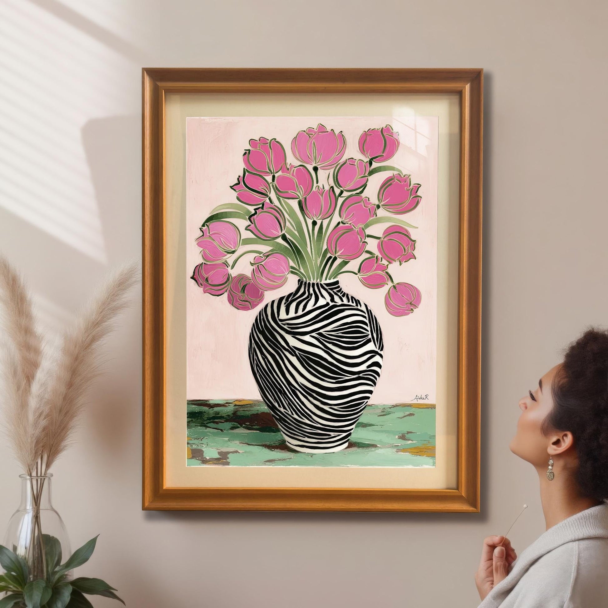 A woman looking up at the framed Zebra Vase and Pink Tulips art print in a gold/orange frame with a mat/mount hanging on a beige wall, next to pampas grass decor.