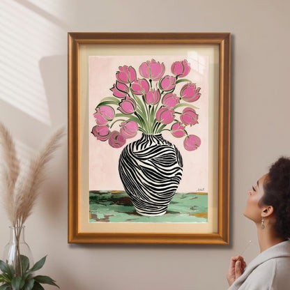 A woman looking up at the framed Zebra Vase and Pink Tulips art print in a gold/orange frame with a mat/mount hanging on a beige wall, next to pampas grass decor.
