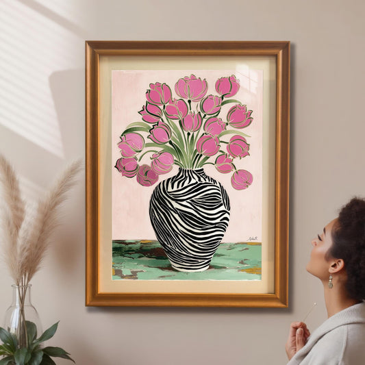 A woman looking up at the framed Zebra Vase and Pink Tulips art print in a gold/orange frame with a mat/mount hanging on a beige wall, next to pampas grass decor.