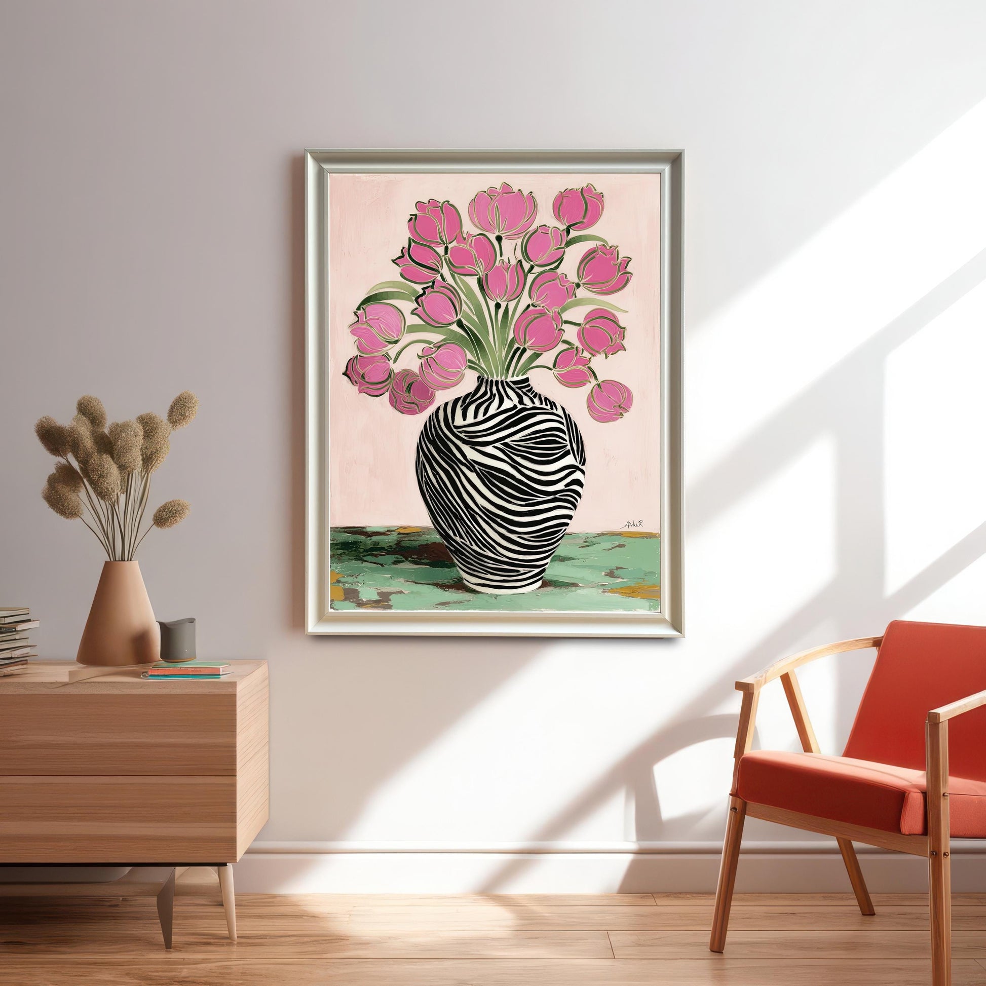 Large framed print of the Pink Tulips and Zebra Vase artwork in a silver/light gold frame without a mat/mount hanging on a light gray wall in a modern room with a wood side table and orange chair.