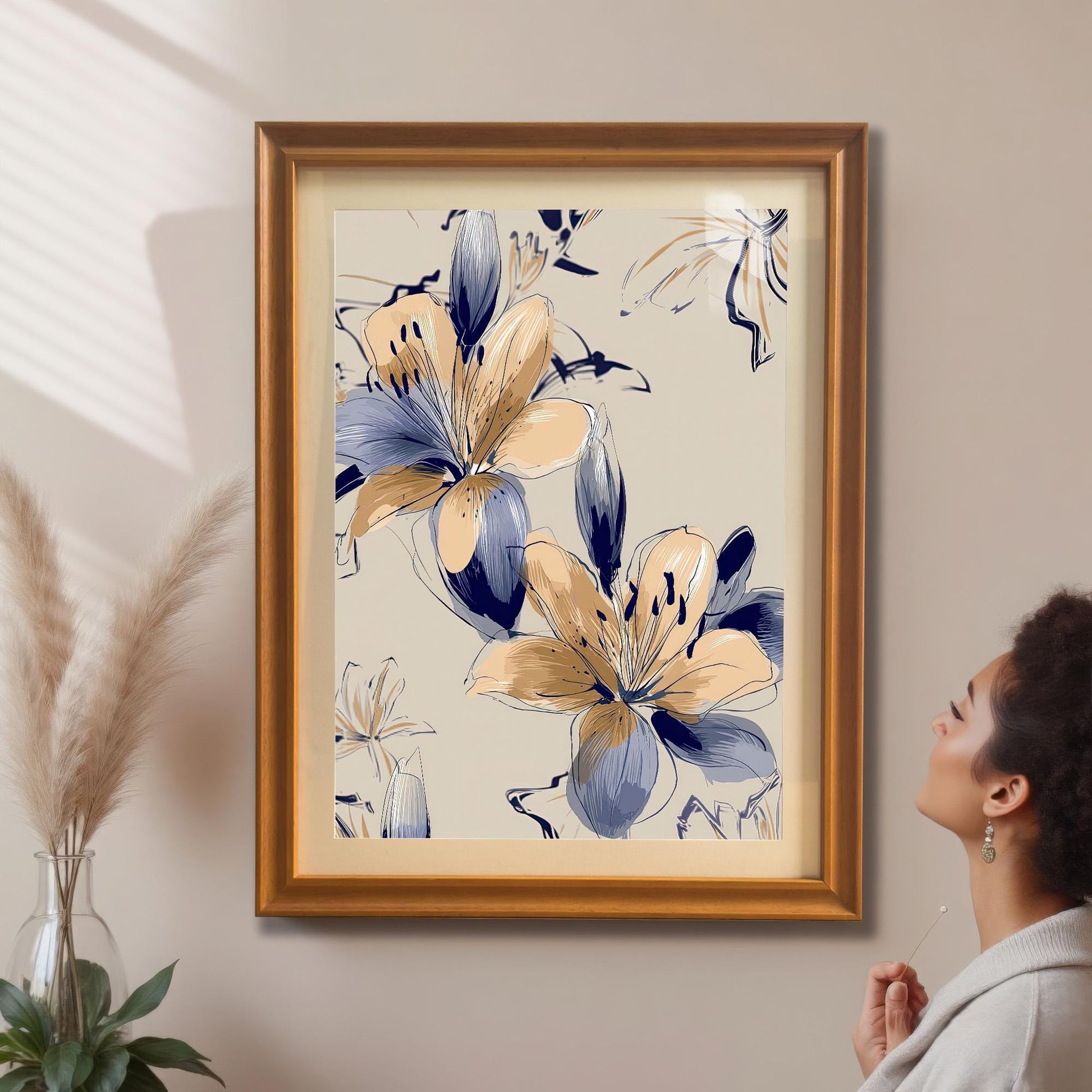 A woman looking up at the framed Navy and Beige Lily print in an orange/gold frame with a mat/mount hanging on a beige wall, next to pampas grass decor.