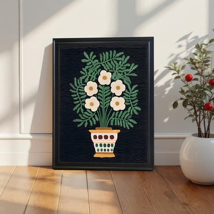 A framed print of the folk floral art in a Black Frame rests on a wooden floor against a white paneled wall, next to a potted plant, highlighting the artwork's dark background contrast.
