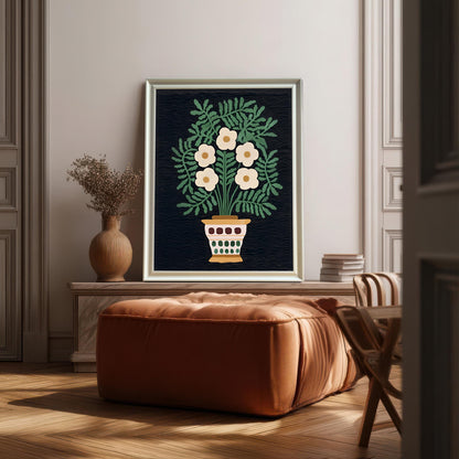 The folk art print of white flowers in a decorative pot hangs on a light-colored wall, framed in a Silver or Light-Colored Frame. It is placed above a leather ottoman and wooden bench in a sunlit room, emphasizing the sophisticated interior style.