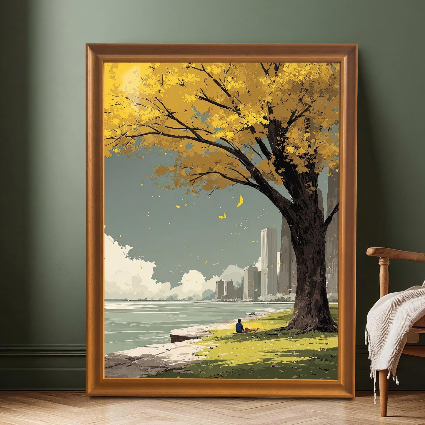 Large, full view of the yellow autumn tree and city skyline art print in a gold/orange frame leaning against a dark green wall on a wood floor next to a chair.