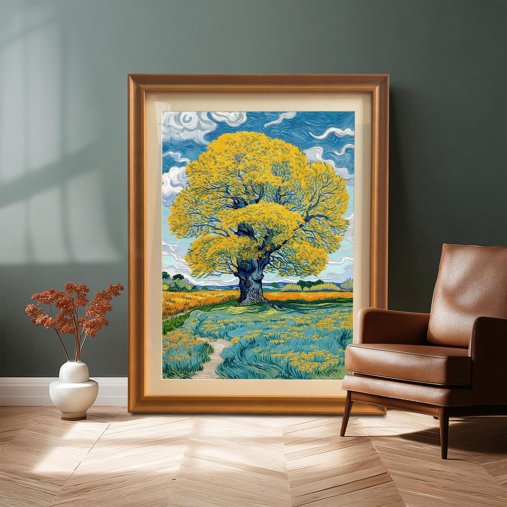 A very large framed print of the yellow tree, with a Coffee-colored frame, leaning on a wood floor against a dark teal wall next to a brown leather armchair.
