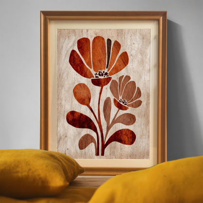 Close-up view of the framed rust-orange floral art print with an orange/gold frame, resting on a wooden surface with a bright yellow pillow in the foreground. (This is a detail/lifestyle shot showing frame color and texture.)