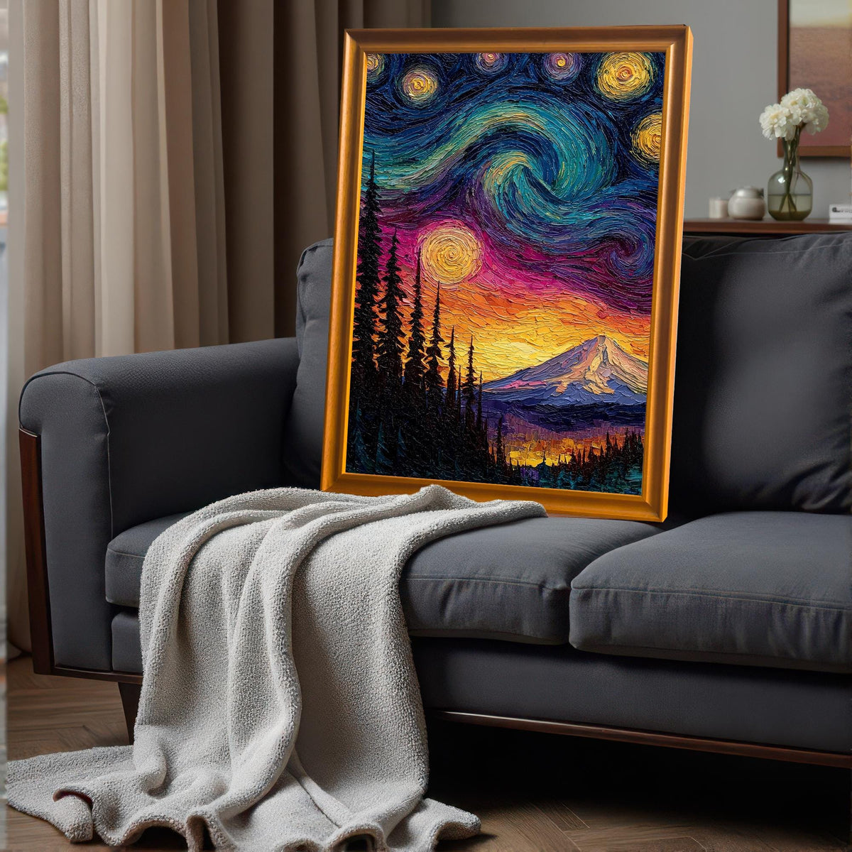 Textured, framed starry night mountain art print in a gold-colored wood frame leaning on a dark gray sofa with a light gray throw blanket in a cozy room.