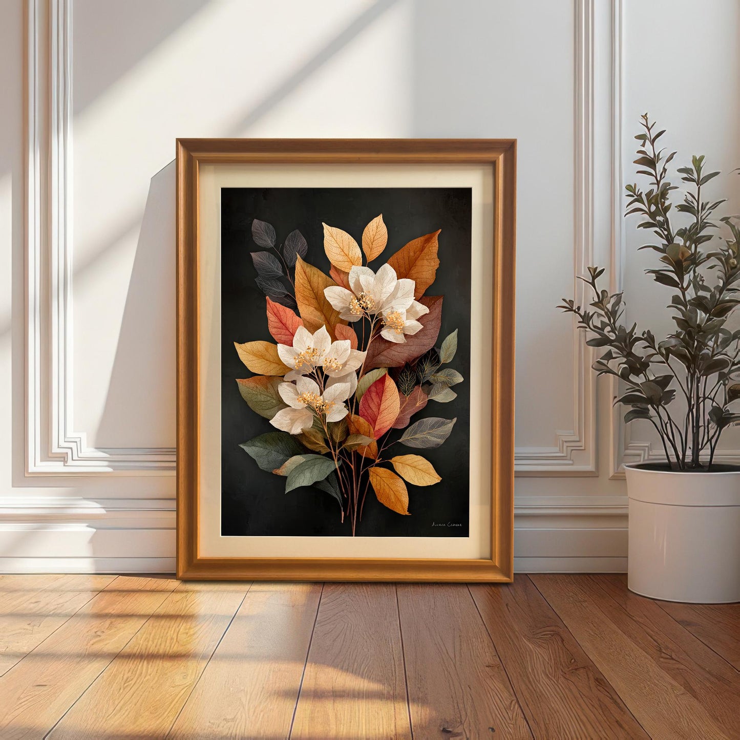 A framed art print featuring a bouquet of white flowers with yellow, orange, and red autumn leaves against a dark background. The print is in an Orange frame with a Mount (matting) and is leaning against a white wainscoted wall next to a potted plant, creating a cozy corner display.