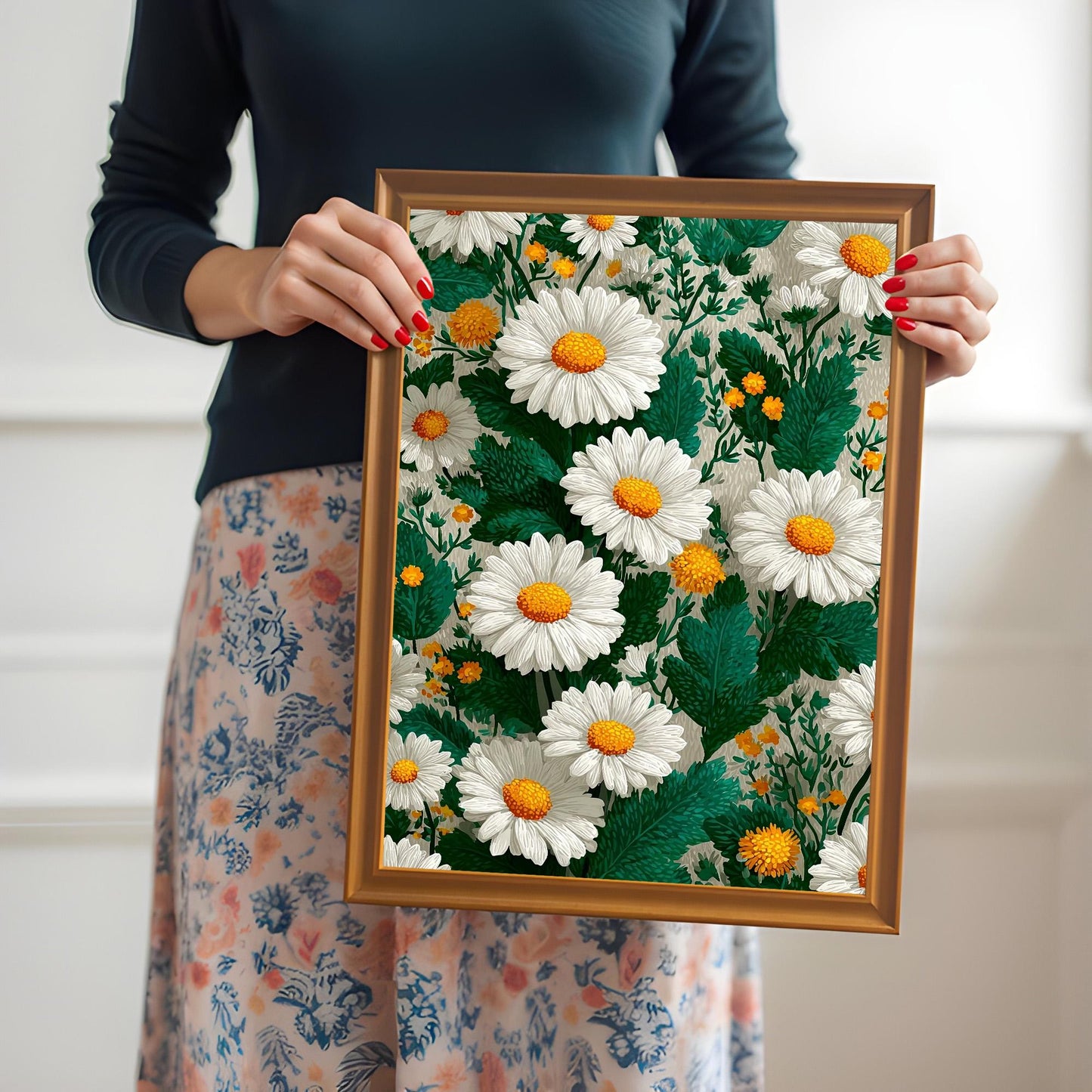 A person holding the framed daisy art print with an orange/gold wood frame to show its scale. The person is wearing a dark top and a floral skirt.