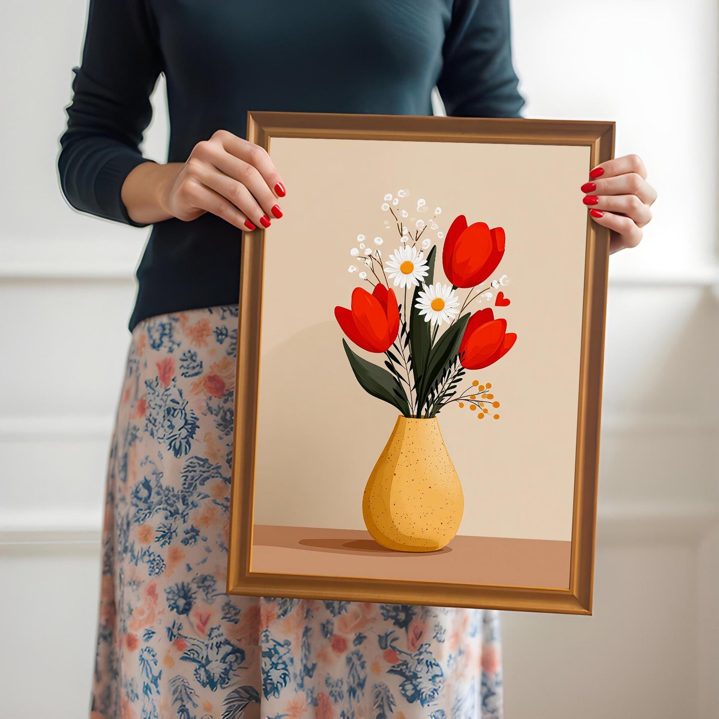 A person holding a framed 'Tulips and Daisies in a Yellow Vase' art print in a brown Orange Frame. The person is wearing a dark top and a floral skirt and has red nail polish.
