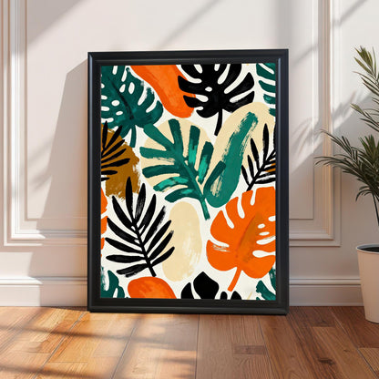 A framed art print featuring a colorful abstract tropical leaf pattern, framed in Black Wood, leaning on a light wood floor next to a potted plant. Sunlight casts shadows across the white paneled wall and floor, highlighting the bright orange, green, black, and beige colors of the artwork.