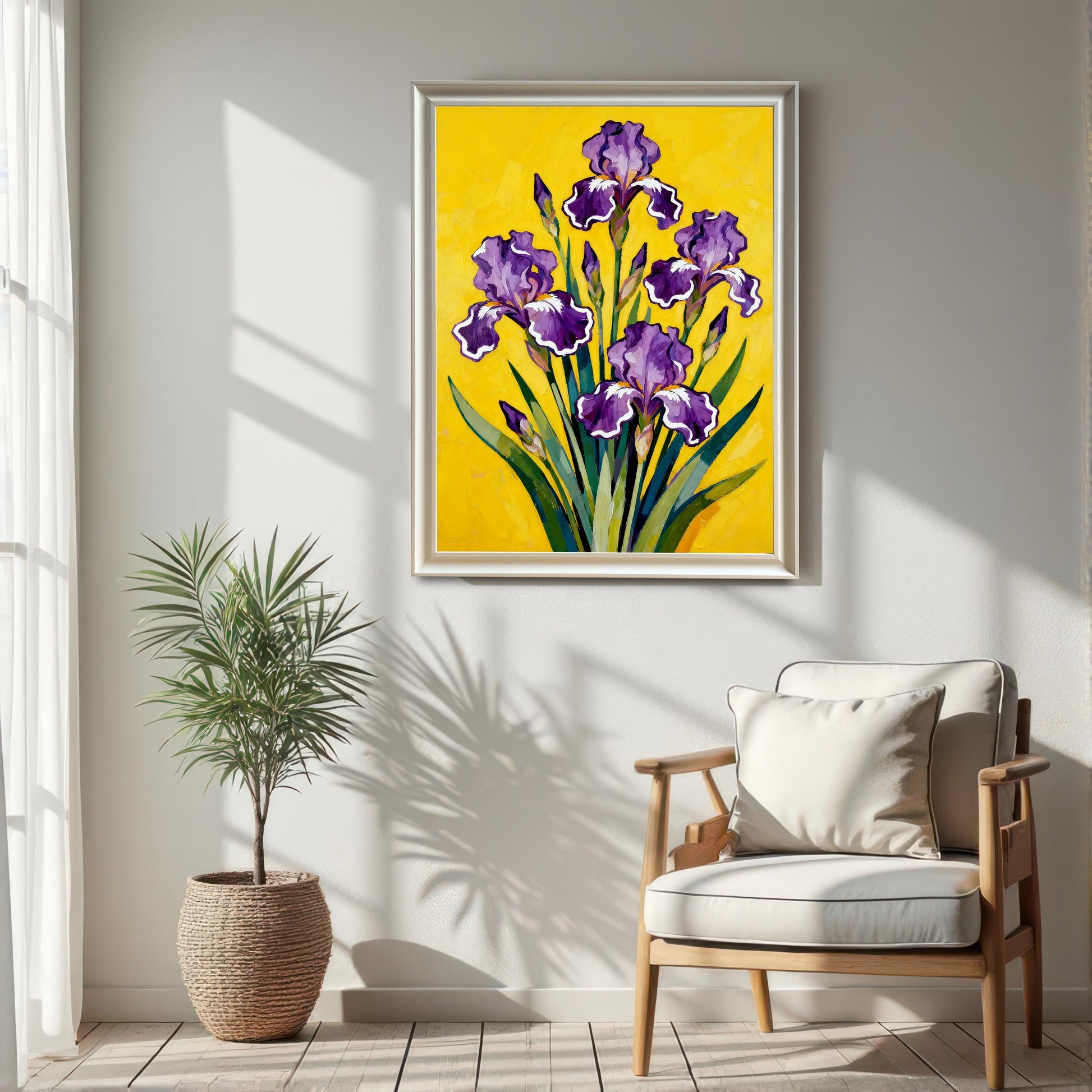 A large White framed art print featuring a vibrant painting of purple Irises on a bright yellow background, hanging on a white wall in a sunlit room above a light wood chair and next to a potted plant in a woven basket.