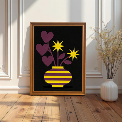 A gold-toned Orange framed art print featuring a purple and yellow striped vase with purple heart-shaped leaves and yellow star flowers on a black background. The framed print is resting on a wood floor against a white paneled wall next to a tall, white vase with dried reeds.