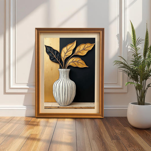 Framed black and gold leaf art print leaning on a wood floor against a white wall with wainscoting. The frame is a gold/orange wood color. A snake plant in a white pot is on the right.