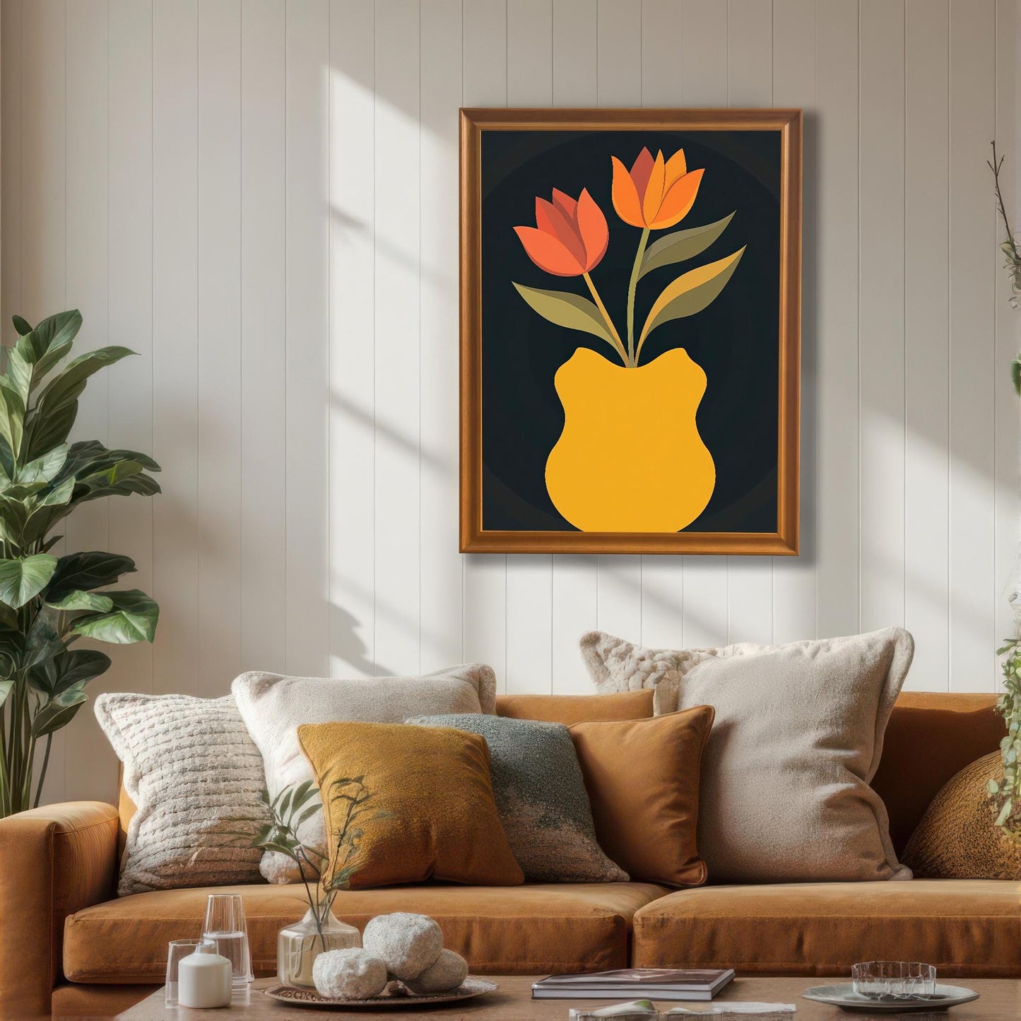 Framed art print of orange and red tulips in a yellow vase, hanging on a white plank wall above a rust-colored couch with multiple pillows. The frame is a gold/orange wood color.