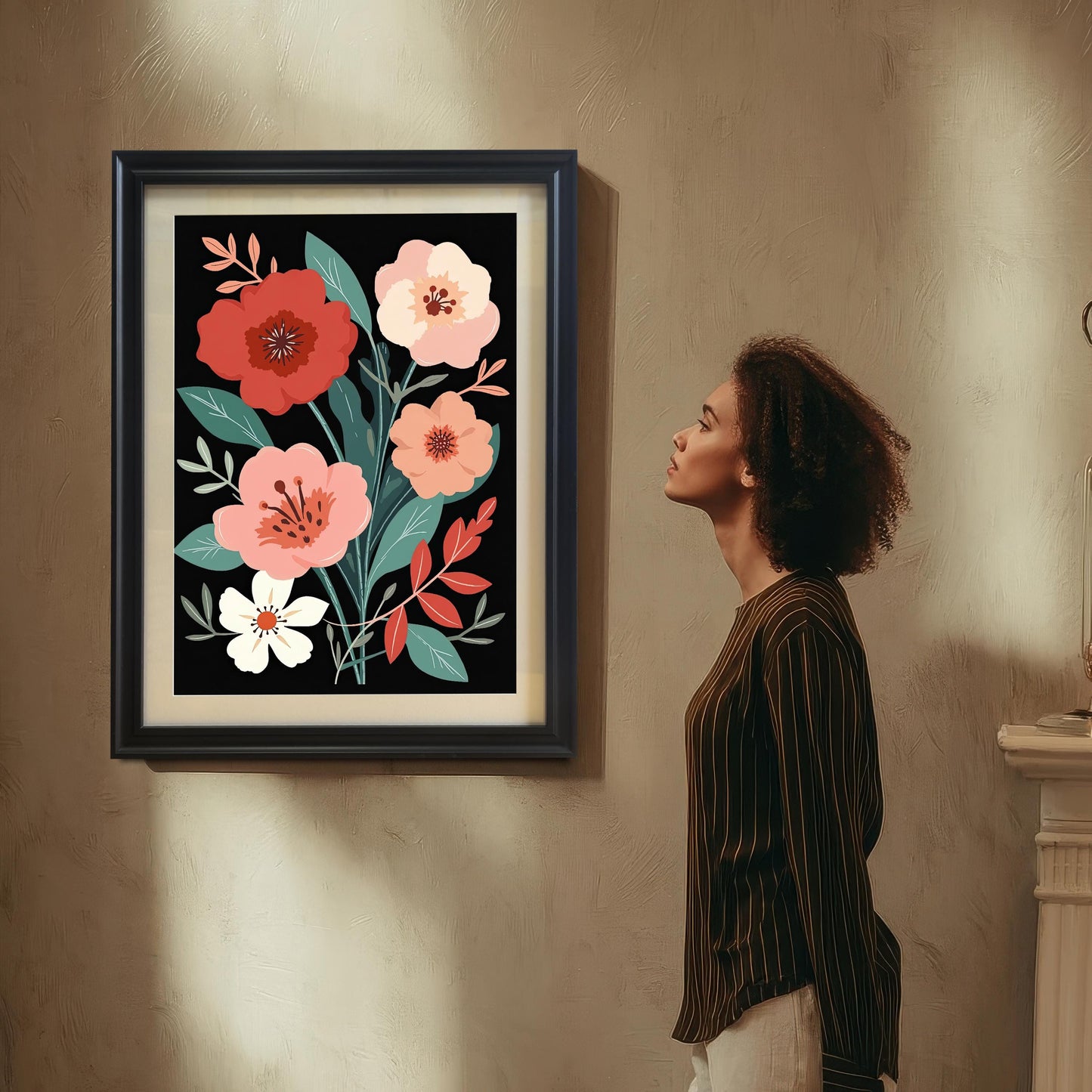 A woman with curly hair, wearing a striped shirt, standing in a dimly lit room and looking up at a framed floral art print hanging on a textured wall. The art has a black frame and a mount (mat).