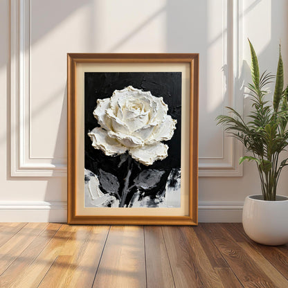 A framed print of the textured white rose painting with an Orange wood frame and a mount (matting), leaning on a wooden floor against a white wall with ornate molding. A potted snake plant is to the right.