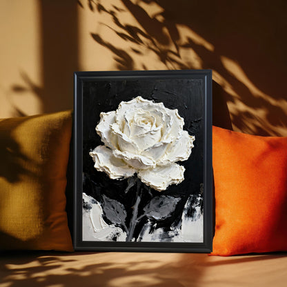A close-up shot of a framed print of the textured white rose painting with a Black wood frame, resting between two mustard yellow and orange pillows. Natural light casts dramatic leaf shadows on the wall behind it.