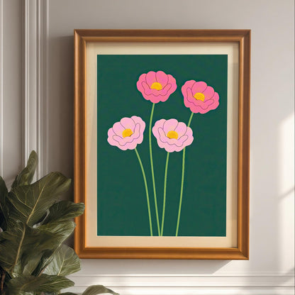The pink floral art print in a warm Orange Frame with a mount/mat, hung on a light grey paneled wall next to a large, dark green houseplant. The art features pink flowers on a dark green background.