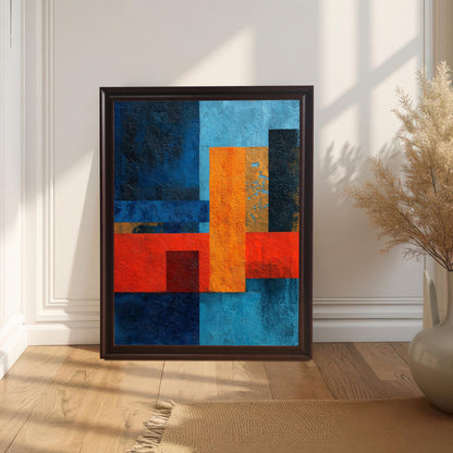 Abstract geometric art print in a dark Coffee wood frame, leaning against a white wall with wainscoting on a light wooden floor with a neutral fringed rug and a vase of dried pampas grass.