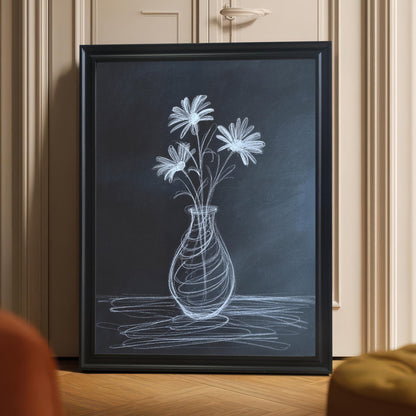 Framed chalk flower print in a black wooden frame leaning on a light hardwood floor against a beige door, with the focus on the artwork. The scene includes hints of orange and yellow accent furniture in the foreground.
