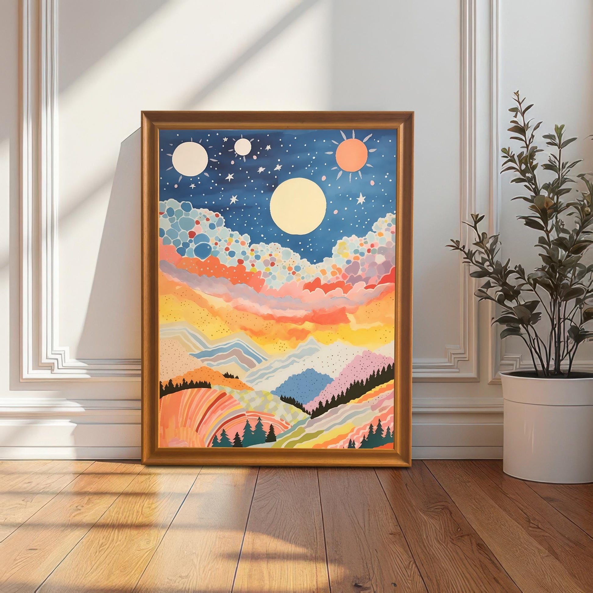 A full-size abstract, colorful celestial mountain landscape art print in a gold/orange wood frame, leaning against a decorative white wainscoted wall next to a potted plant. The artwork features a starry blue sky and warm, colorful hills.