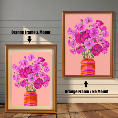 Comparison image showing the Cosmos flower print with an Orange Frame & Mount (matting) on the left, and an Orange Frame / No Mount on the right, against a white paneled wood wall.