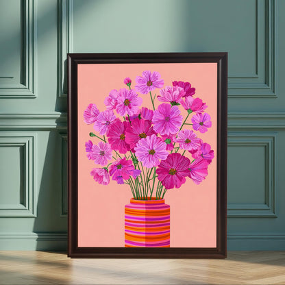 Vertical image of a framed art print featuring bright pink and magenta Cosmos flowers in a striped orange vase on a pink background. The print is in a dark frame, leaning against a teal/green paneled wall.