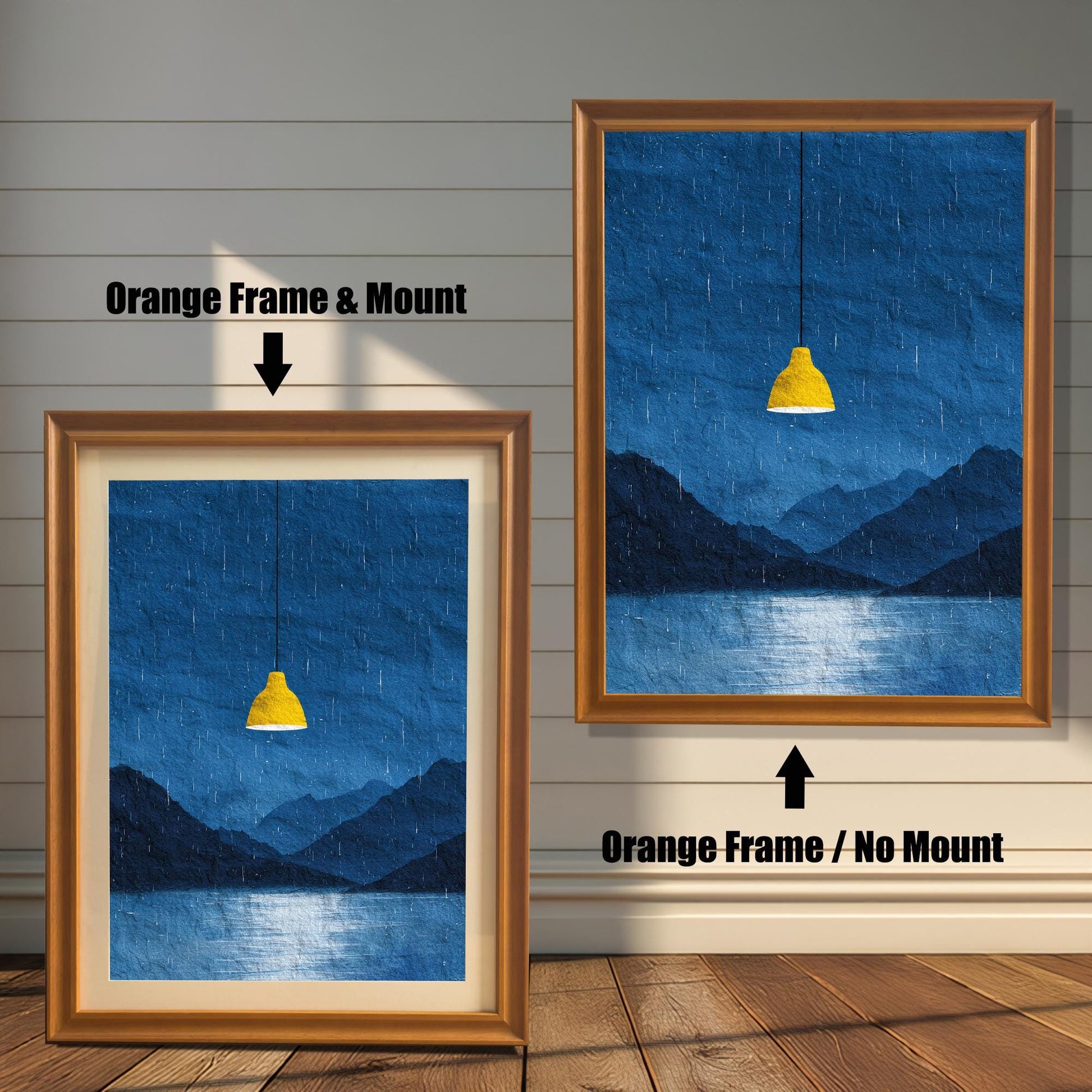 A comparison image showing two framed art prints on a wooden wall. The print on the left is in an Orange Frame & Mount (golden/orange frame with a light mat). The print on the right is in an Orange Frame / No Mount (golden/orange frame, no mat). Both feature the dark blue rainy landscape with the yellow lamp.