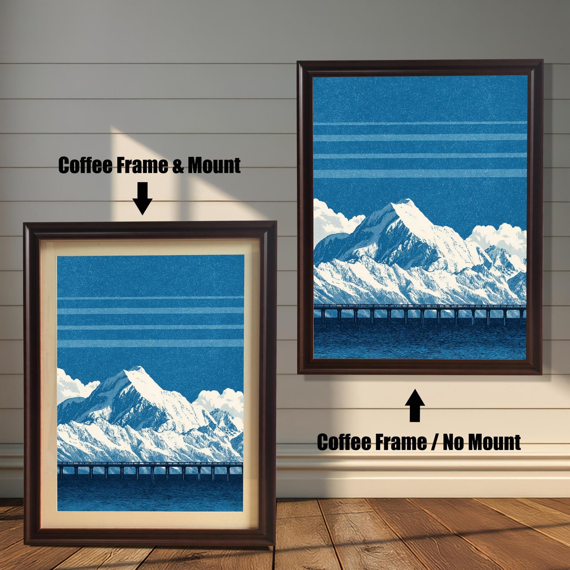 comparison image showing two framed art prints on a wooden wall. The print on the left is in a Coffee Frame & Mount (dark brown frame with a light mat). The print on the right is in a Coffee Frame / No Mount (dark brown frame, no mat). Both feature the blue mountain and bridge design.