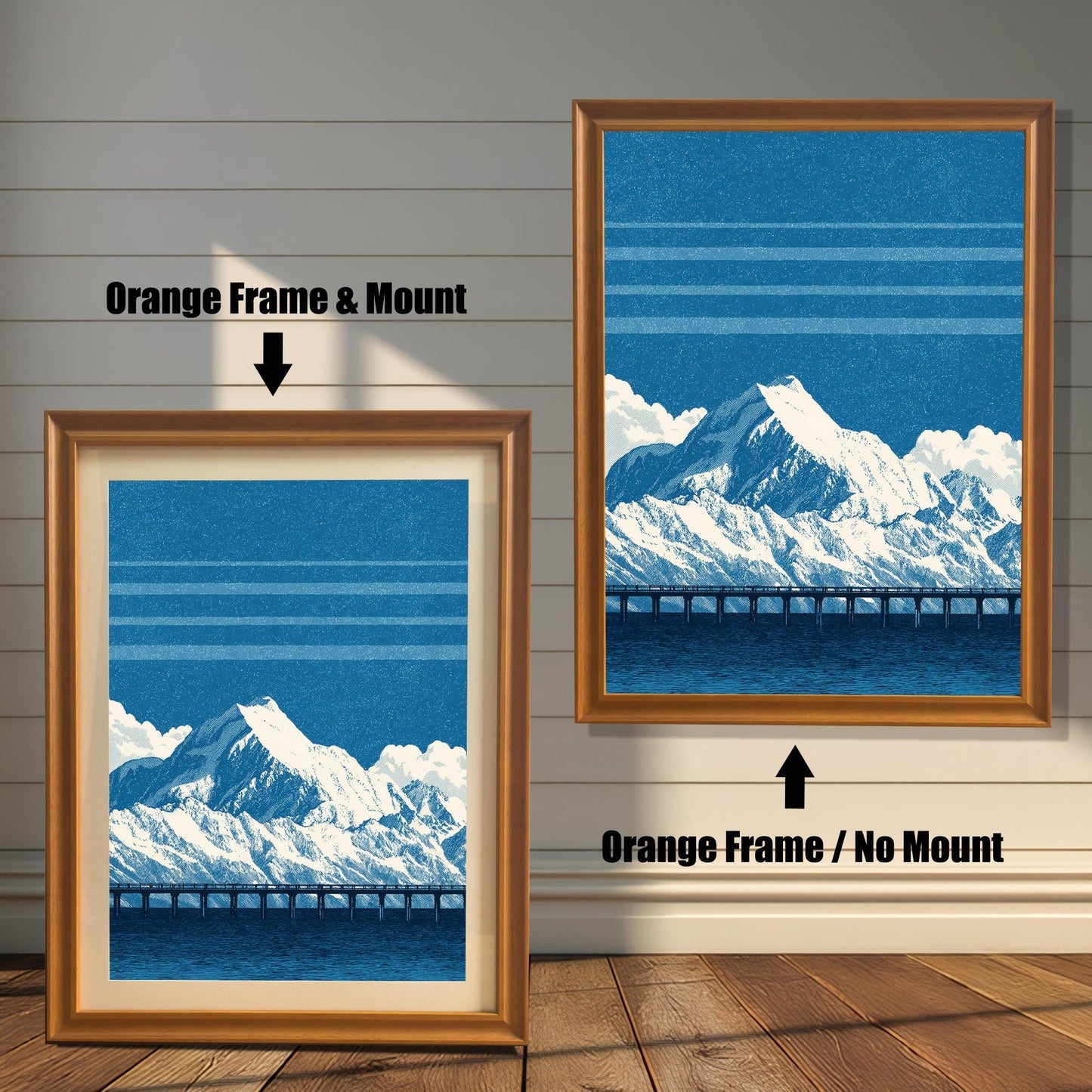 A comparison image showing two framed art prints on a wooden wall. The print on the left is in an Orange Frame & Mount (golden/orange frame with a light mat). The print on the right is in an Orange Frame / No Mount (golden/orange frame, no mat). Both feature the blue mountain and bridge design.