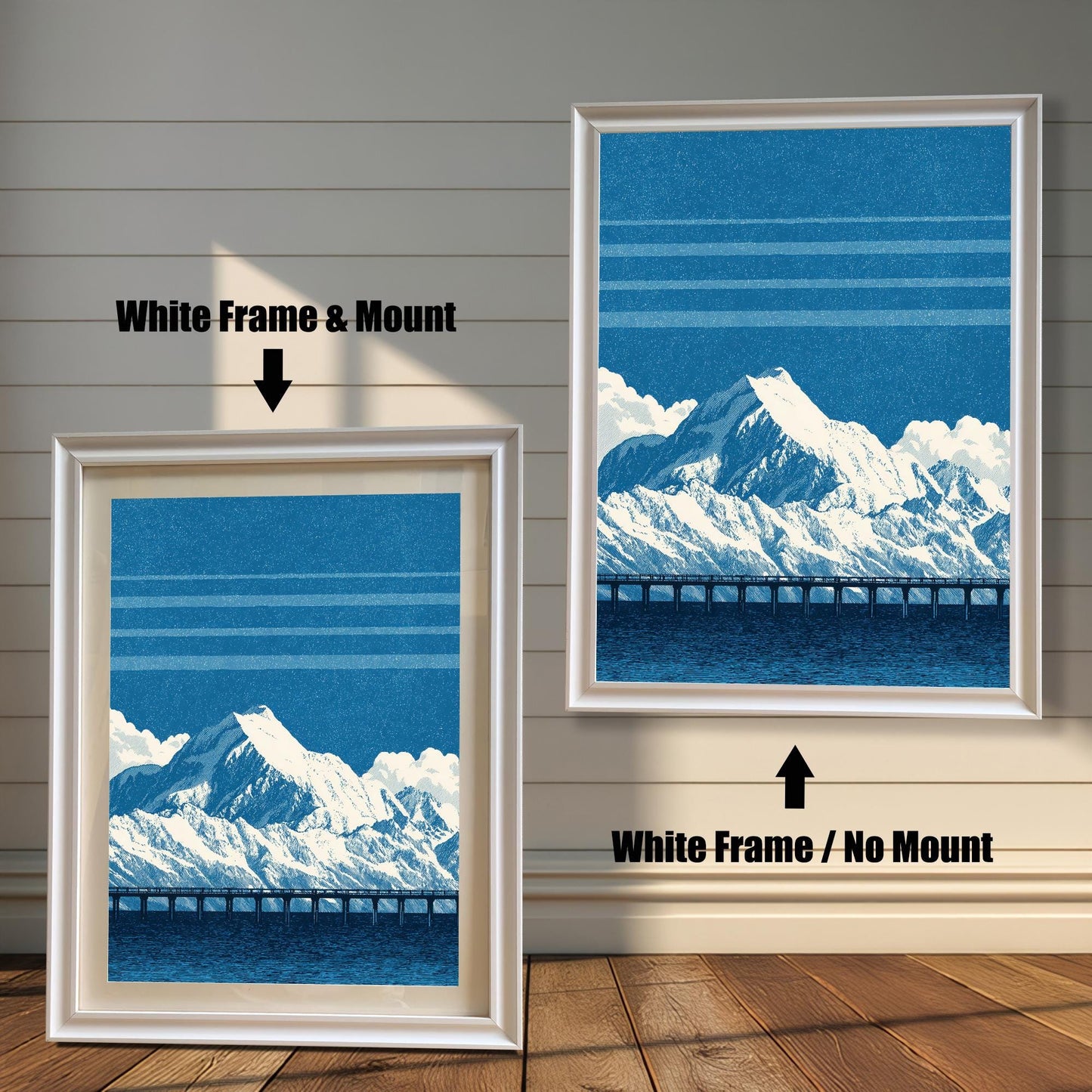 A comparison image showing two framed art prints on a wooden wall. The print on the left is in a White Frame & Mount (white frame with a light mat). The print on the right is in a White Frame / No Mount (white frame, no mat). Both feature the blue mountain and bridge design.