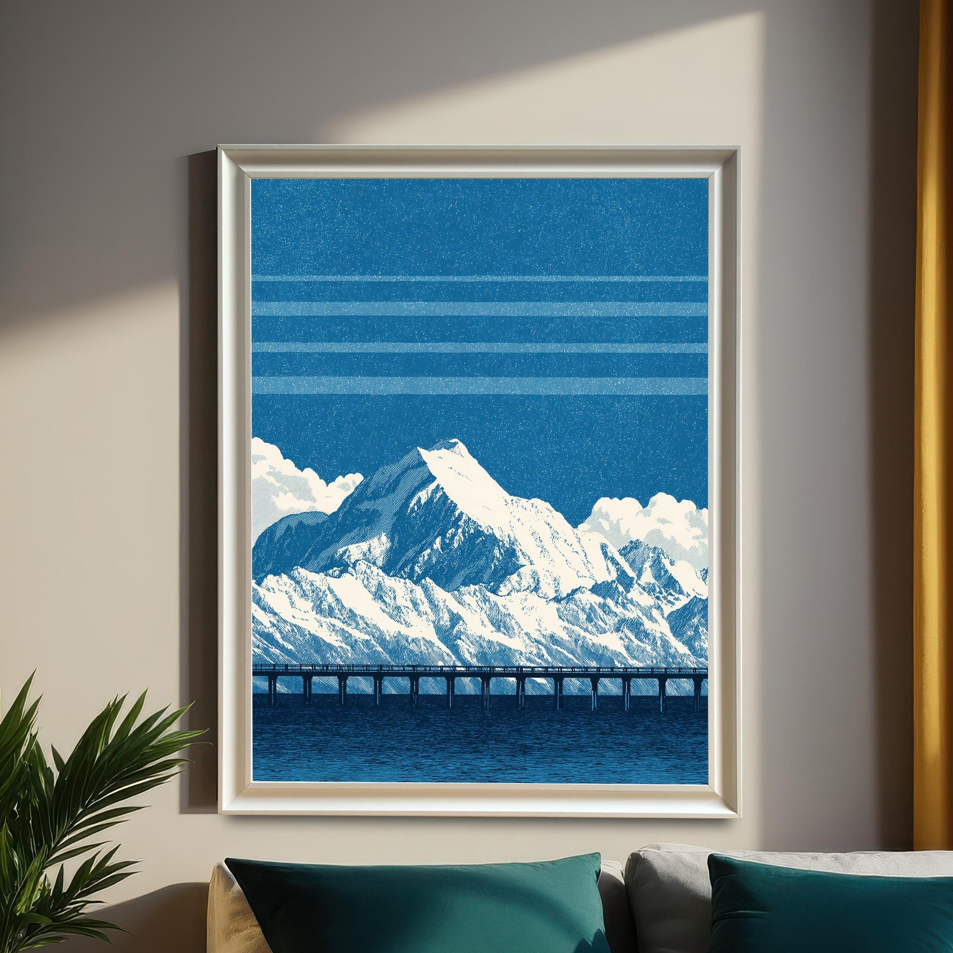 The blue mountain and bridge art print in a white frame, hanging on a beige wall above a bed. Dark teal and white pillows, a dark curtain, and a potted plant on a side table complete the moody bedroom setting.