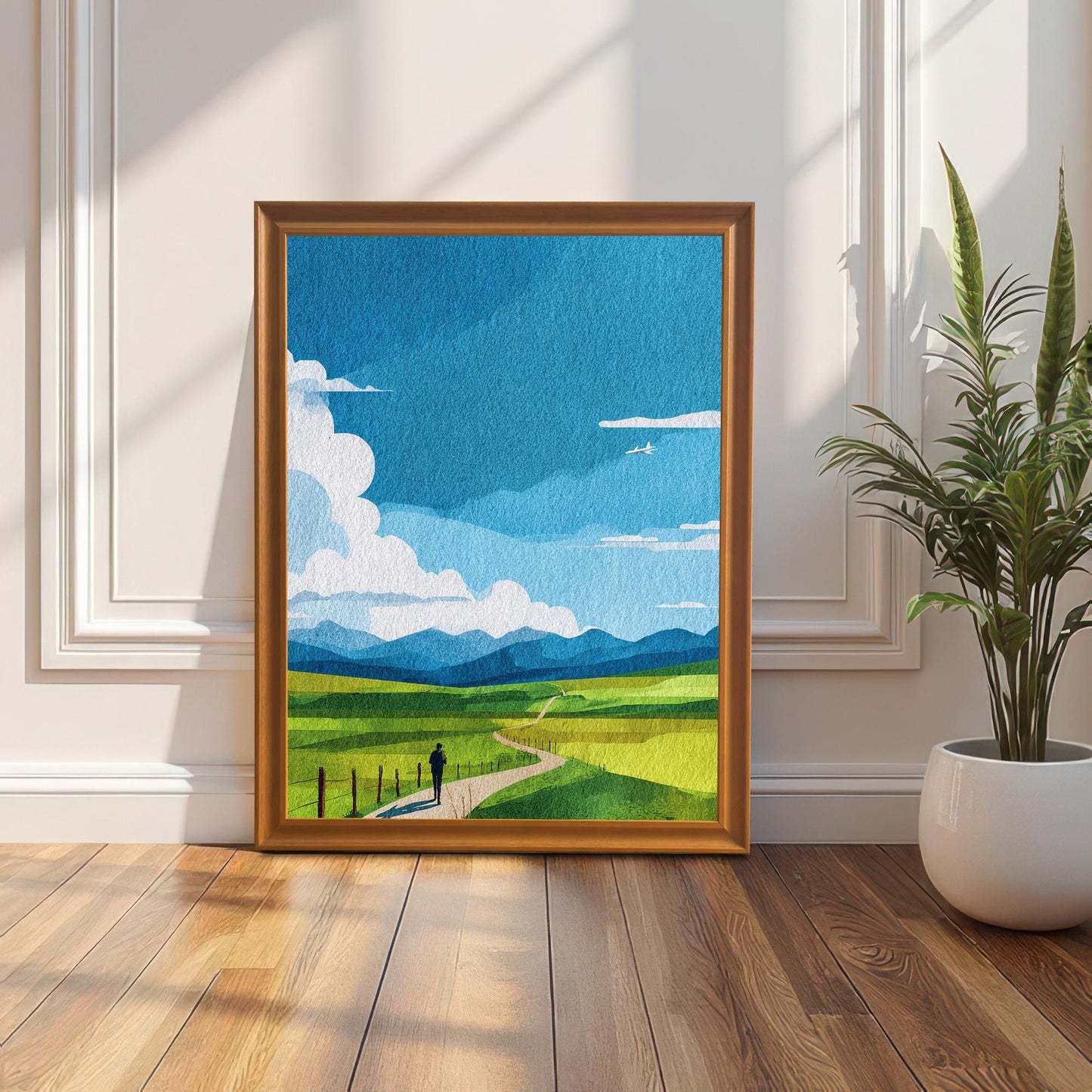 Art print of the green field and blue sky landscape in an Orange/light brown wood frame (no mount), leaning on a sunlit wooden floor against a white paneled wainscoting wall. A snake plant in a white pot is on the right.