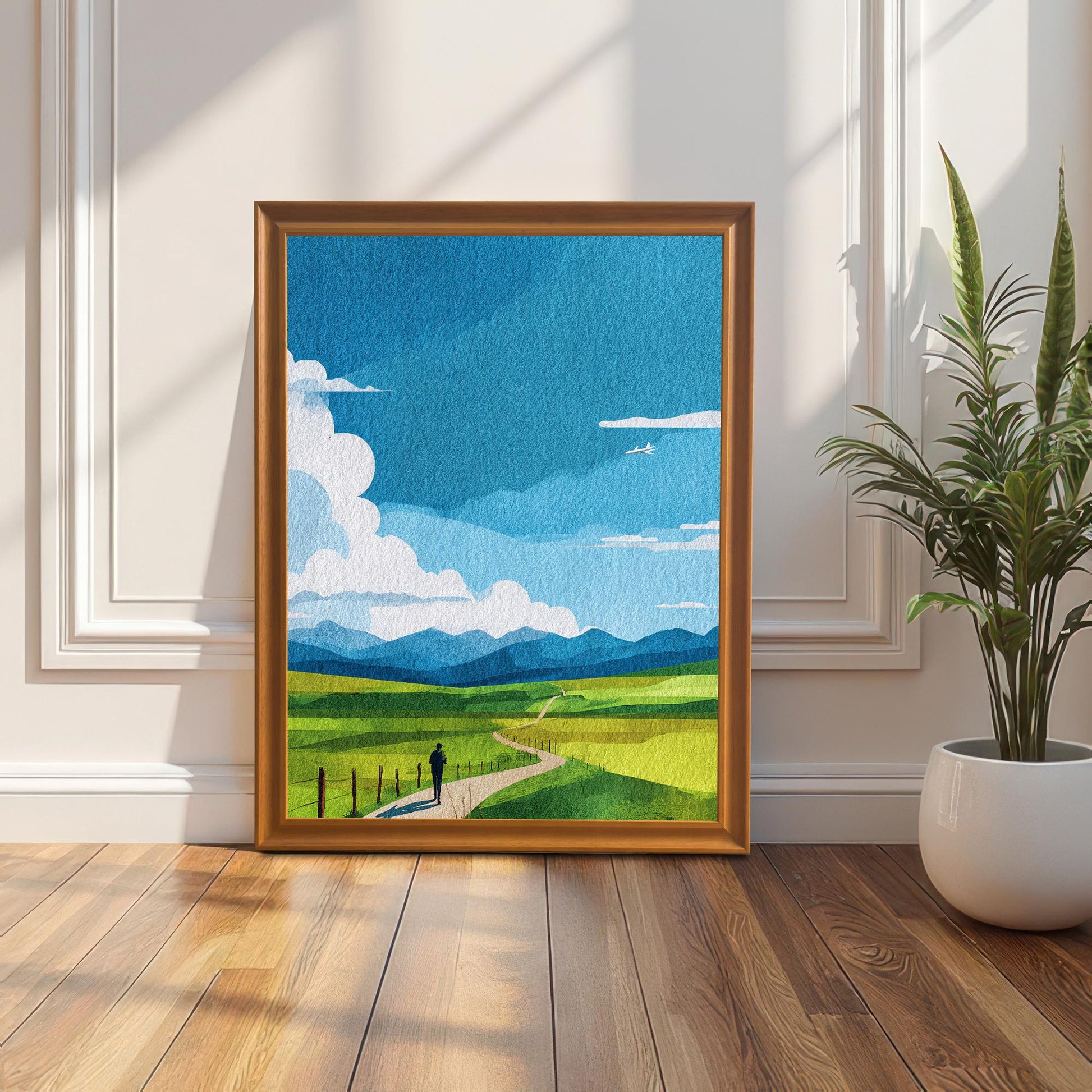 Art print of the green field and blue sky landscape in an Orange/light brown wood frame (no mount), leaning on a sunlit wooden floor against a white paneled wainscoting wall. A snake plant in a white pot is on the right.