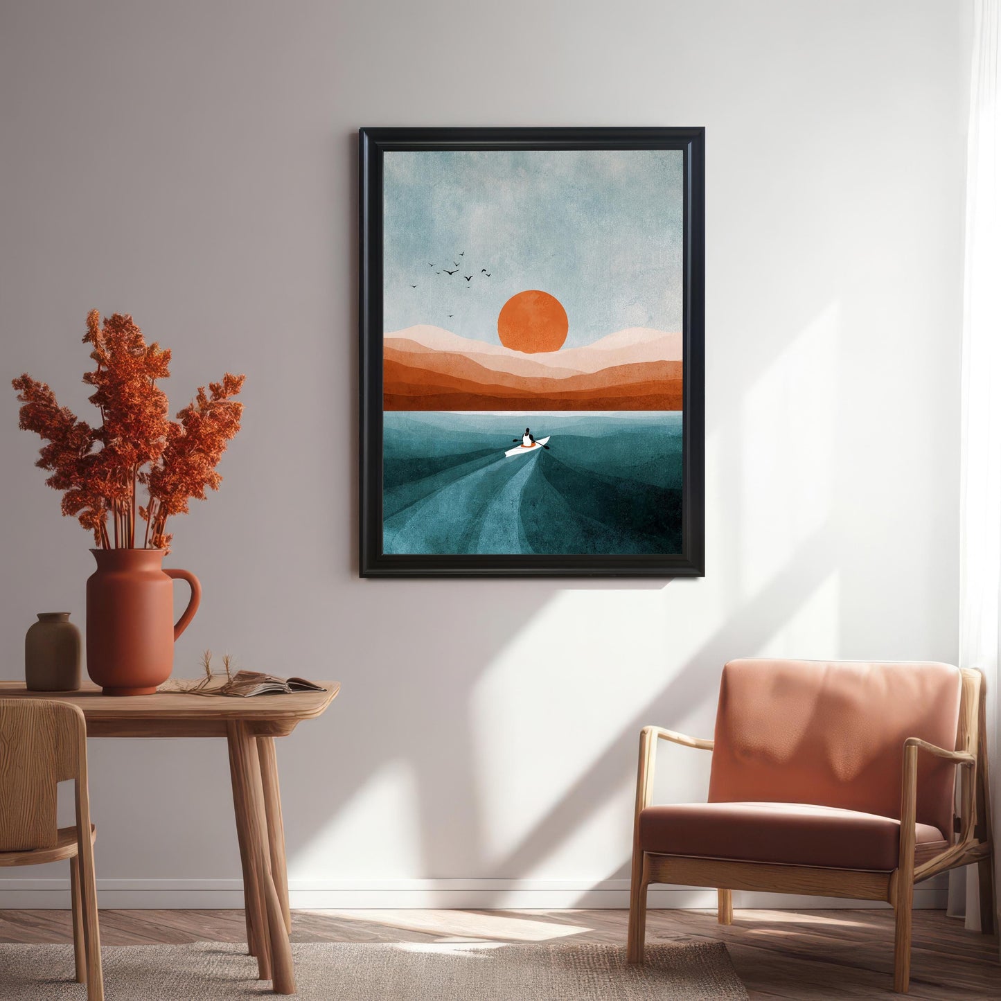 Art print in a black frame hanging on a white wall in a modern dining or living space. Features a wooden side table, a terracotta vase with dried orange flowers, and a light orange upholstered wooden chair.