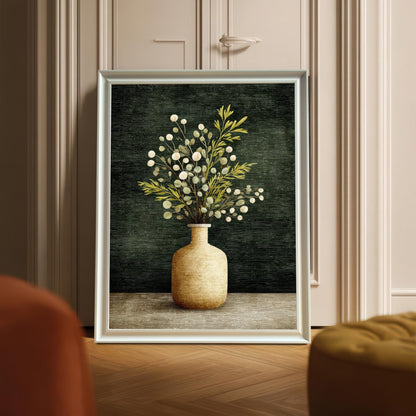 A framed art print of a vase with foliage, displayed leaning against a door with decorative molding. The frame is a White wood.