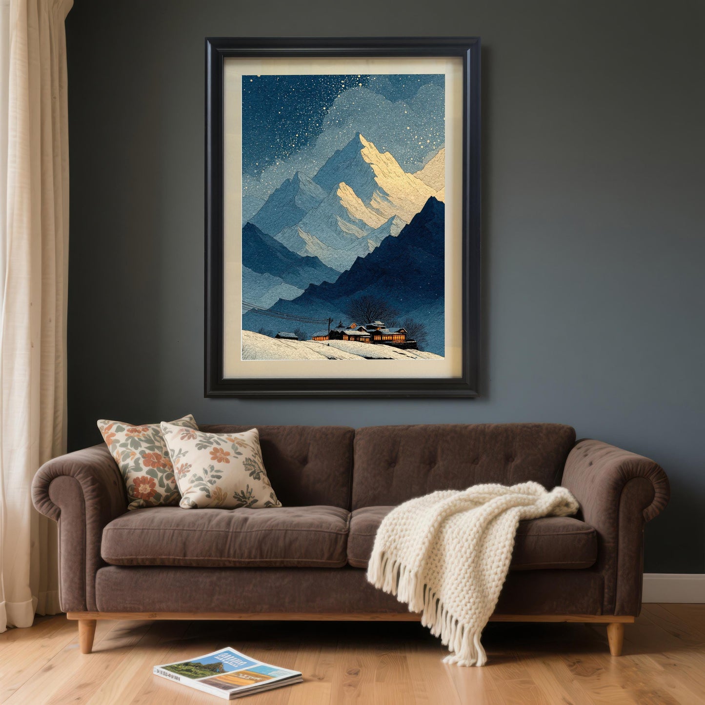 A large framed art print of the snowy mountain landscape hanging above a brown sofa with floral pillows and a white blanket. The frame is Black with a light border/mount. The walls are dark gray.