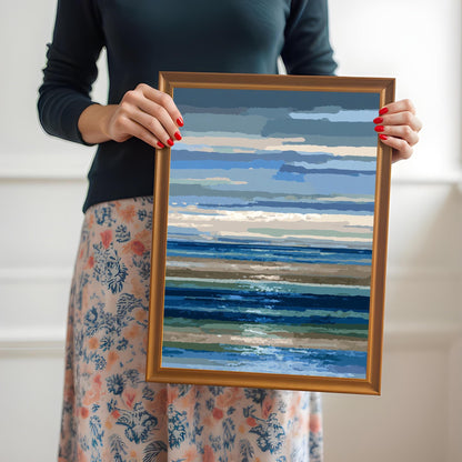 A woman in a dark shirt and floral skirt holding the abstract blue and brown striped seascape print in a gold/orange wood frame.