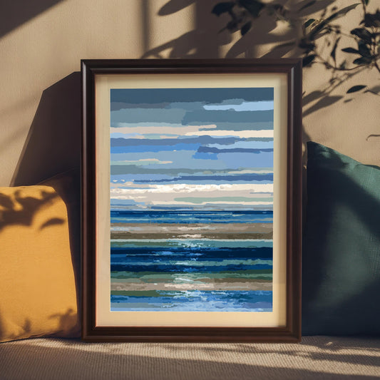 Abstract blue and brown striped seascape art print in a dark frame with a mount, resting on a sofa between a yellow and a teal pillow, with dappled shadows on the wall.