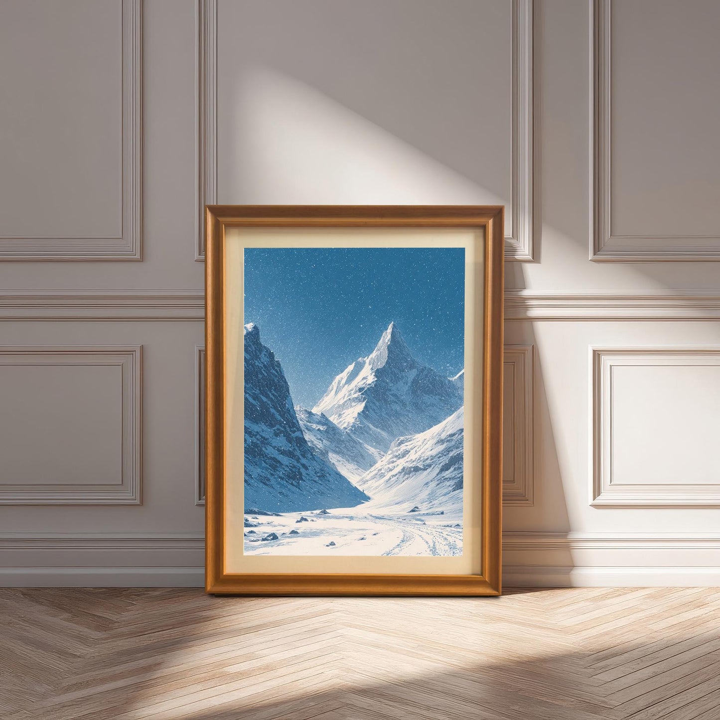 Snowy mountain valley print in a gold/orange wood frame with a mount, leaning against a white paneled wall on a wood floor, illuminated by sunlight.