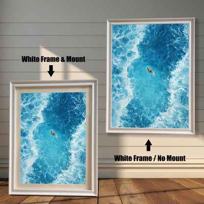 Comparison of the ocean art print with a White frame. The image on the left has a 'Mount' (mat board) and is leaning against the wall. The image on the right is hanging and has 'No Mount'. Both have a white wood frame.