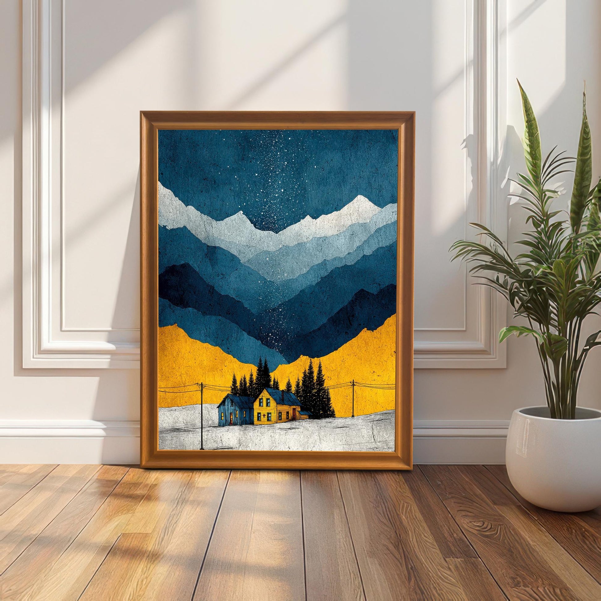 The framed art print, featuring a snowy mountain scene with a yellow and blue house under a starry night sky, leaning against a white wainscoted wall on a wooden floor in a sunlit room. The frame is Orange (or light wood).